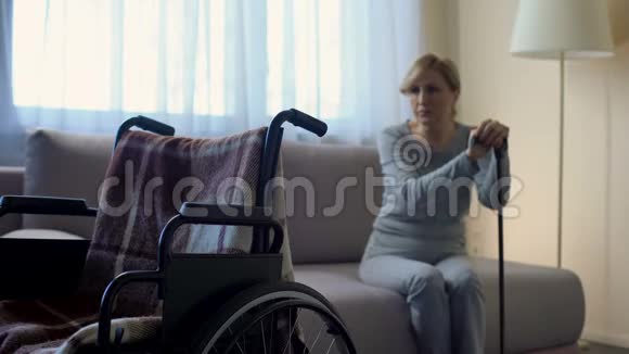 孤独的残疾妇女坐在沙发上看着空荡荡的轮椅回忆视频的预览图