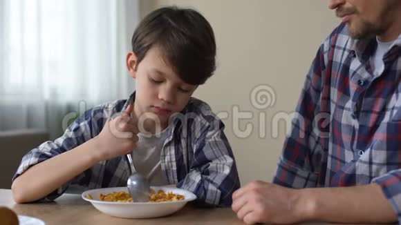 可怜的小男孩用勺子搅拌玉米片看着父亲胃口很差视频的预览图