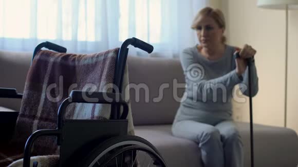 坐在沙发上看着轮椅康复中心的沮丧的女性退休人员视频的预览图