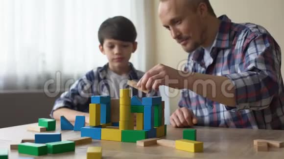 可爱的爸爸和他微笑的儿子在家玩彩色玩具立方体童年视频的预览图