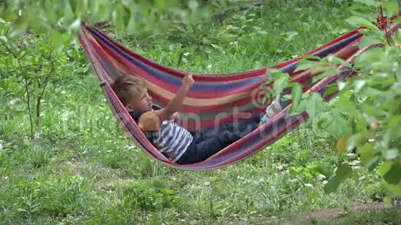 可爱的小男孩在绿色自然的彩色吊床上放松视频的预览图