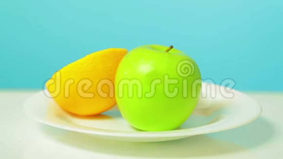 整个绿色的苹果一半的猕猴桃和橘子放在一个白色的盘子里旋转成一个圆圈视频的预览图