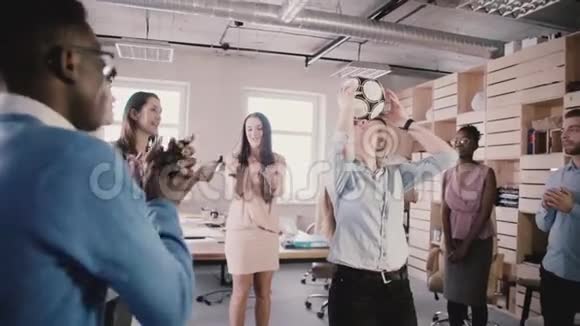 在现代时髦的办公室里一个欧洲女孩头朝下玩足球多种族的同事庆祝鼓掌慢动作视频的预览图