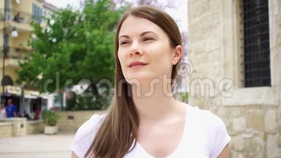 慢动作在欧洲城市一位身穿白色t恤面带微笑的年轻女子走在街上环顾四周视频的预览图