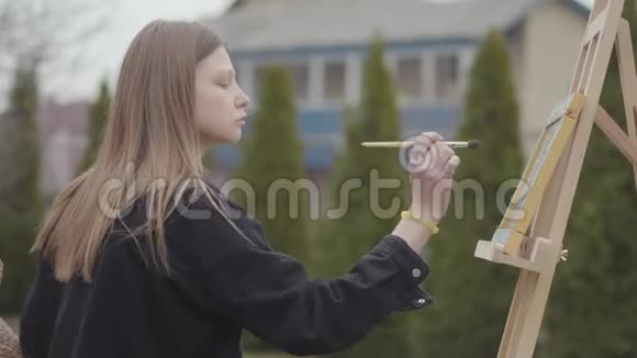 漂亮的年轻吸烟女孩坐在后院的户外画布上画画充满激情的成功艺术家视频的预览图