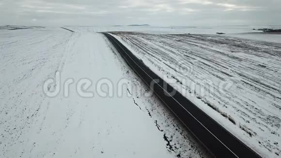 冬天的道路上白雪覆盖的田野背景下鸟瞰车辆移动视频的预览图