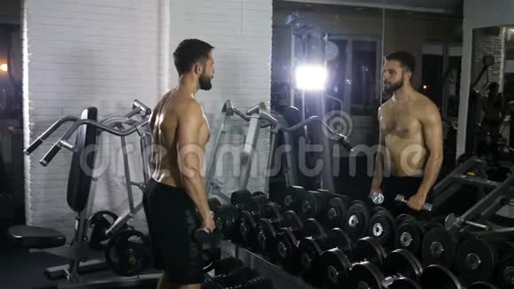 一个体格健壮的人在对面的健身房里用哑铃训练双手的肌肉视频的预览图