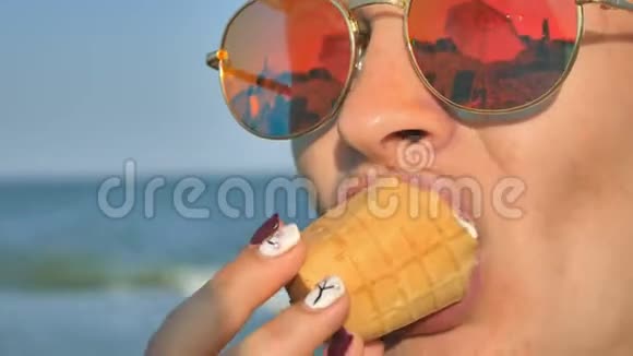 年轻的黑发女人在海滩上舔着冰淇淋蓝色的海洋背景和太阳镜视频的预览图