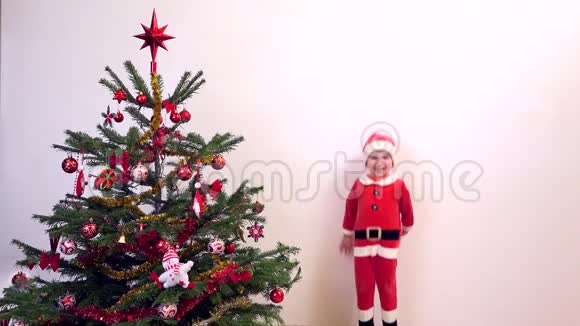 穿着圣诞老人衣服的快乐孩子在圣诞树旁跳跃等待礼物视频的预览图