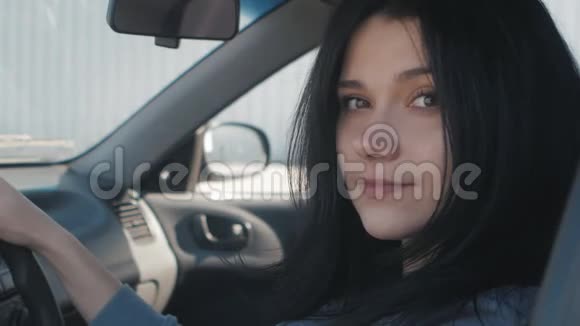 一个可爱的年轻女子坐在驾驶座的方向盘后面的车里的特写照片视频的预览图