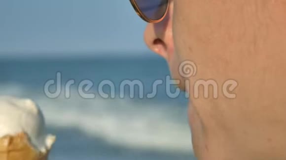 年轻的黑发女人在海滩上舔着冰淇淋蓝色的海洋背景和太阳镜视频的预览图