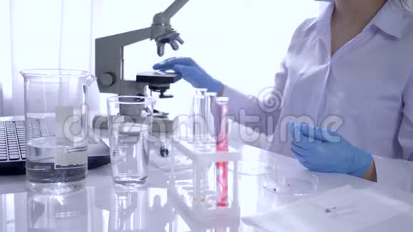 医学实验室拿着注射器样本的妇女做血液测试用小瓶看着桌子上的显微镜视频的预览图