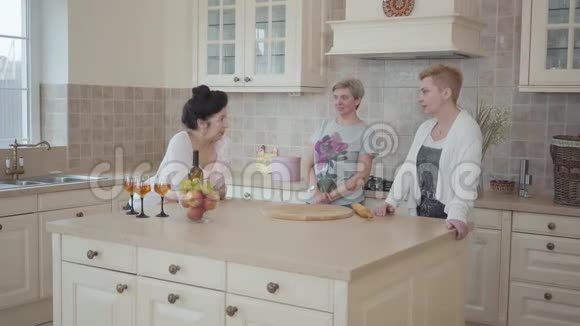 三个成熟的女人在家里聊天站在厨房中间的现代桌子附近高级妇女视频的预览图