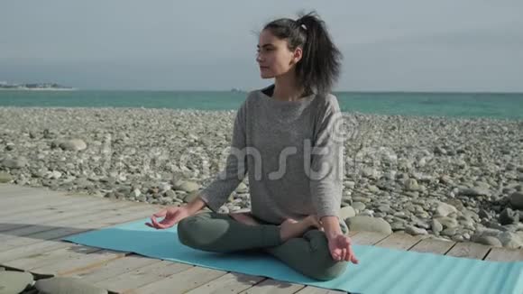 年轻的黑发女子坐在海边的莲花位置上沉思视频的预览图
