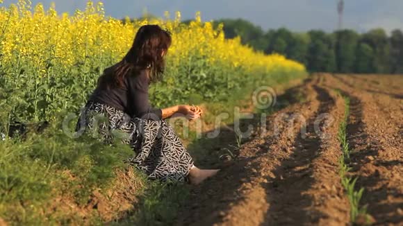 一位有花的单身女士坐在一片春暖花开的田野旁视频的预览图