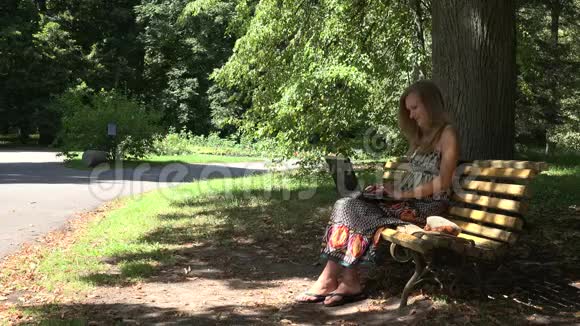 学生女孩工作与笔记本电脑坐在绿色公园的长凳上4K视频的预览图