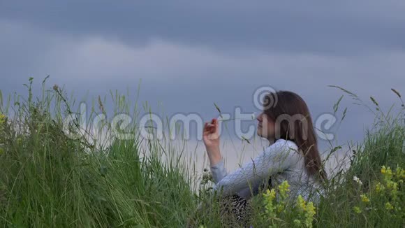 美丽的年轻女子在嬉戏闻着一朵雏菊山顶接近蓝天视频的预览图
