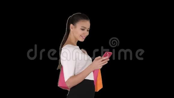 美丽的年轻女子用手机走路拿着购物袋阿尔法频道视频的预览图