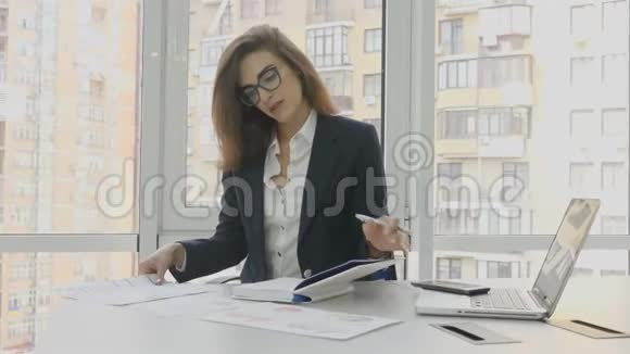 办公室工作人员戴眼镜的女商人坐在办公室的扶手椅上在办公室里检查文件和写作任务视频的预览图