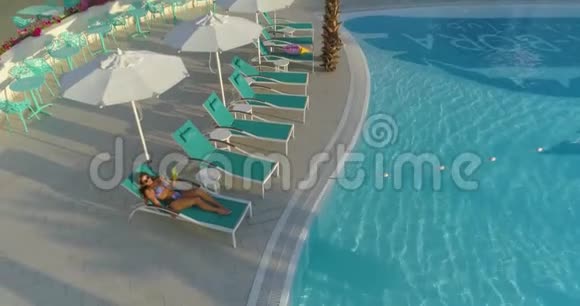 空中美丽的女孩躺在游泳池旁的休息室里视频的预览图