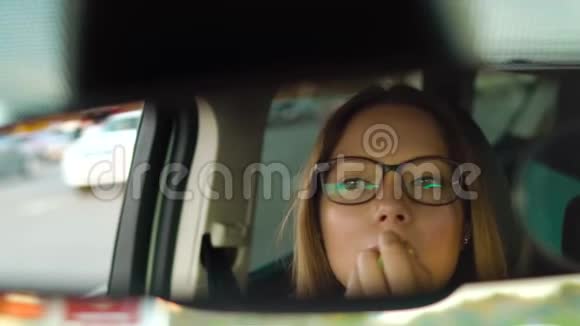 戴眼镜的漂亮女孩在车里画嘴唇在镜子里检查她的外表视频的预览图