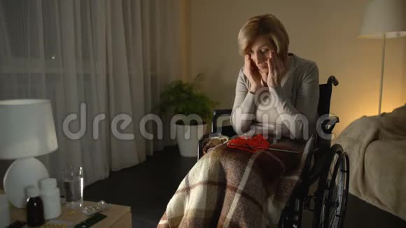 坐在轮椅上的老疲惫的女人戴着眼镜试图编织视力很差视频的预览图