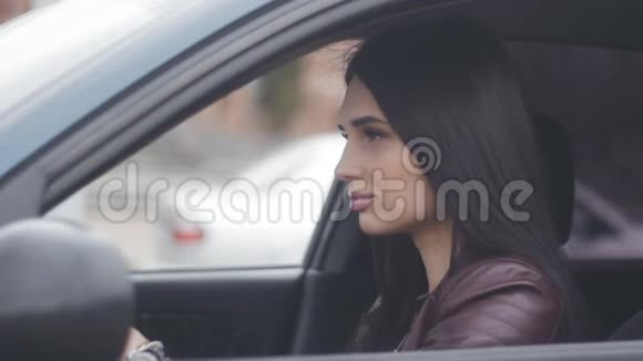 美丽的黑发女人坐在汽车上坐在城市驾驶座上视频的预览图