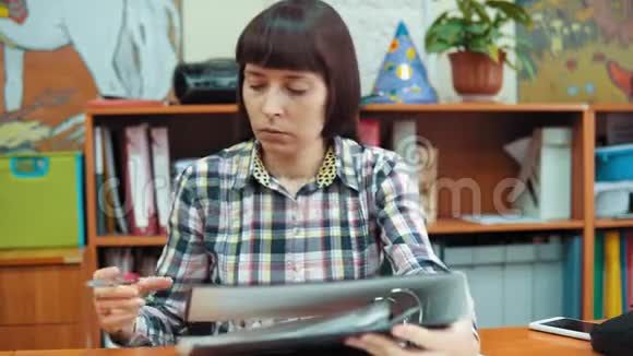 年轻的女教师坐在桌边处理文件视频的预览图