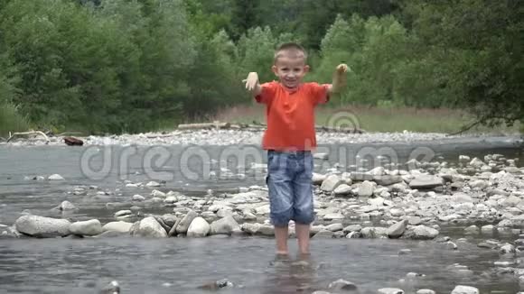 快乐的孩子在山河里玩耍孩子用手和脚泼水笑着笑着的男孩视频的预览图