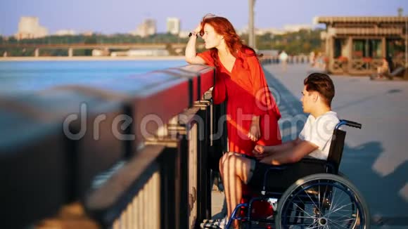 夏天晚上坐轮椅的男人和红头发的女孩在海滨交流视频的预览图