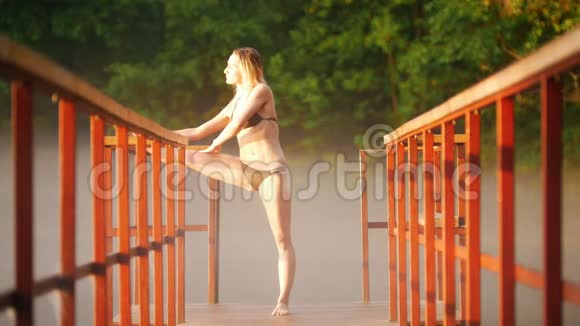 在桥上的湖边游泳前做热身运动的年轻女子视频的预览图