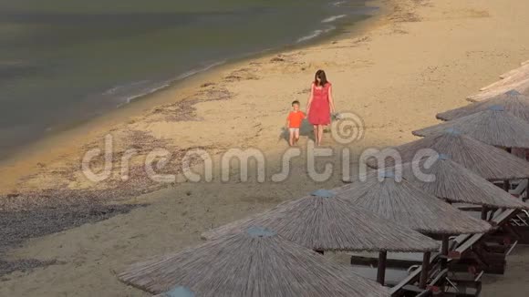美丽的母亲牵着小儿子的手赤脚走在沙滩上傍晚视频的预览图