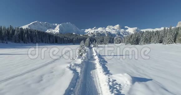 在阳光明媚的一天飞越一条雪域的乡间小路俯瞰群山视频的预览图