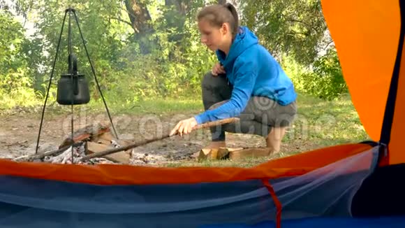 从一个旅游帐篷里看一个女人把木柴放在火上在上面加热水壶视频的预览图