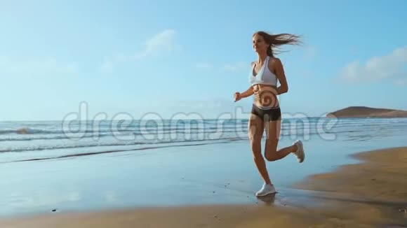 美丽的运动女性穿着白色运动鞋沿着美丽的沙滩奔跑健康的生活方式后视图慢视频的预览图