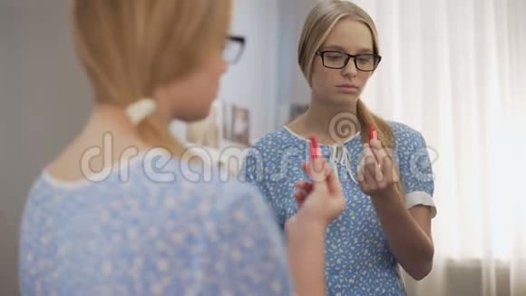 戴眼镜的女青少年在镜子旁尝试第一支红色口红长大了视频的预览图