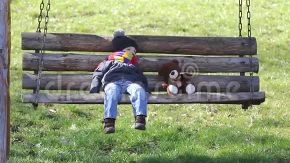 小男孩和泰迪熊在公园的平衡椅上放松美丽的春日视频的预览图