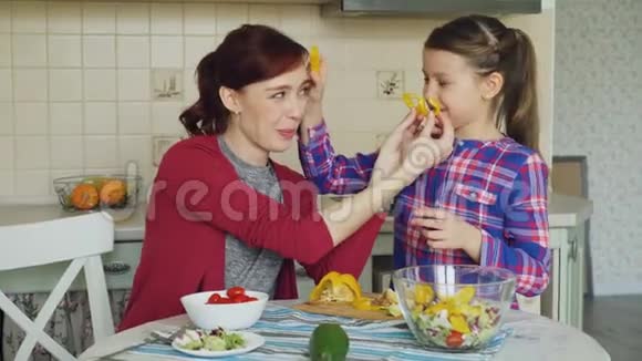 快乐的母亲和快乐的女儿在做菜的时候玩着做鬼脸傻乎乎地吃蔬菜看着镜头视频的预览图