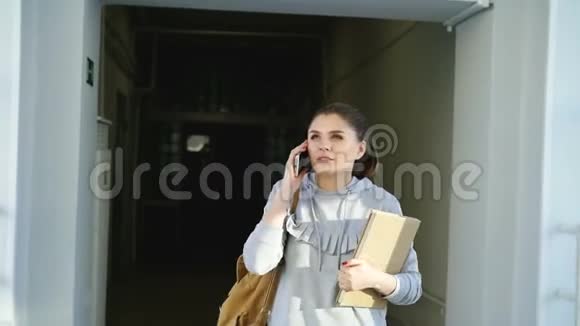 多莉拍摄的美丽美丽的女学生走在大学走廊上拿着课本在电话交谈视频的预览图