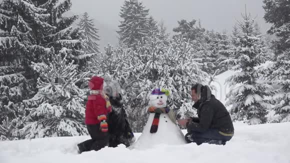 一家人在公园里堆雪人可爱的孩子固定纽扣下雪的树美丽的冬天的家庭肖像真正的团队合作视频的预览图