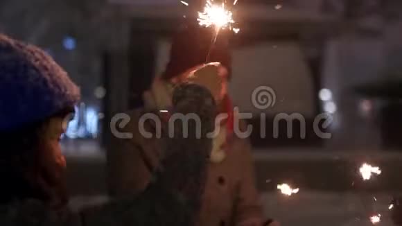 快乐的朋友用手中的火花玩得开心人们在冬天的夜晚在大雪纷飞的圣诞节市场上跳舞视频的预览图