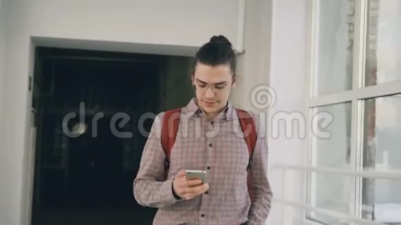 年轻英俊的白种人时髦的男学生拿着电话走在大学里白色的宽敞走廊里视频的预览图