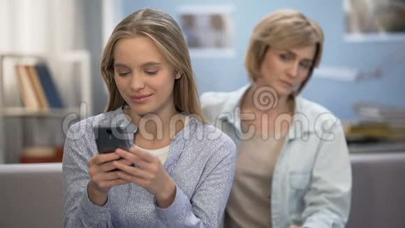 快乐的少女在智能手机上发短信悲伤的母亲坐在沙发上视频的预览图