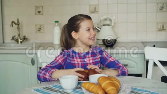 快乐的母亲和女儿坐在桌子旁分享松饼玩得很开心同时在家里在厨房吃早餐视频的预览图