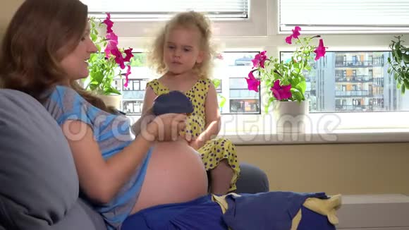 准妈妈和她可爱的女儿在女人肚子上玩婴儿帽视频的预览图