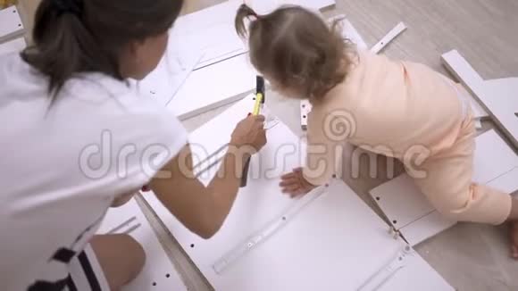 妈妈和女儿收集一个盒子一个女人正在用螺丝刀组装一个白色的木柜视频的预览图