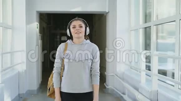 戴着耳机的漂亮迷人的女学生正在走廊上和她的队友们会面给她五个人视频的预览图
