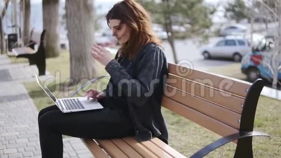 20的迷人女性穿着时髦的都市服装坐在长凳上在笔记本电脑上打字视频的预览图