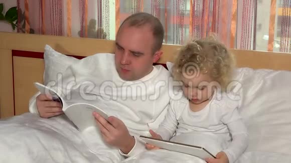可爱的小女孩带着平板电脑和秃头父亲看书视频的预览图