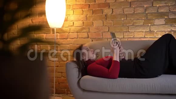 躺在室内沙发上用平板电脑发短信的年轻白种人女性特写镜头视频的预览图